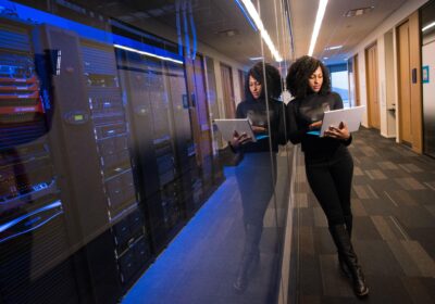 Blog Woman on a laptop standing beside server room